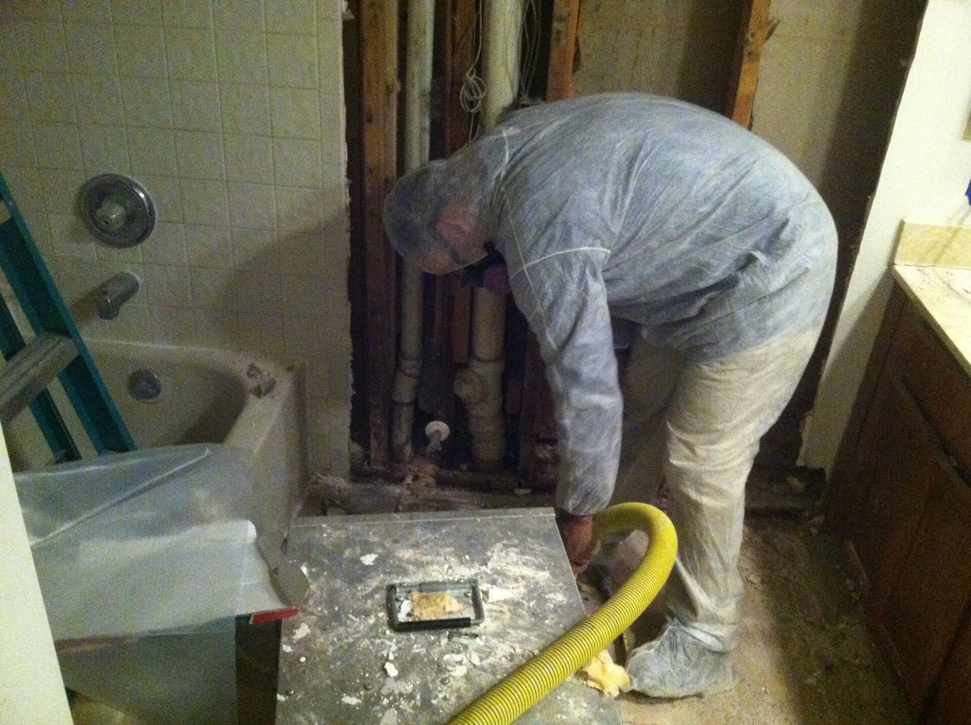 Fresh Air technician in a protective suit removing water-damaged drywall behind a bathtub