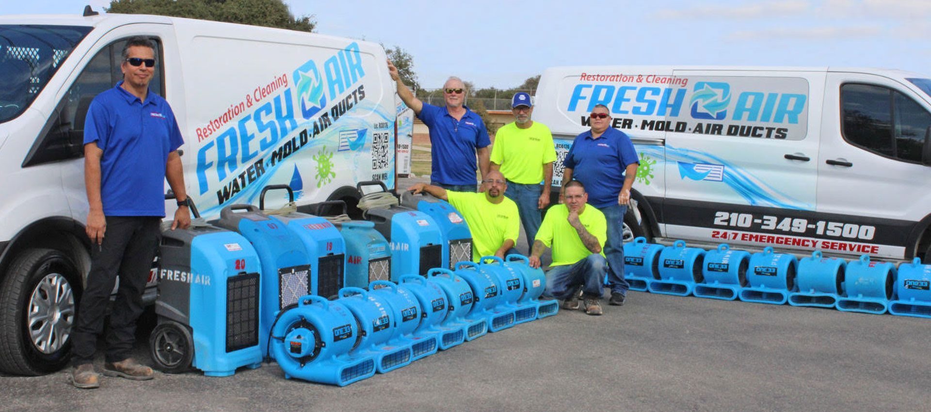Five Fresh Air crew members standing with two service vans and a row of blue air movers