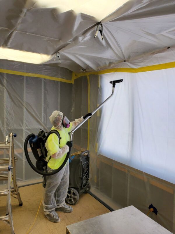 Technician in a protective suit spraying antimicrobial inside a sealed containment