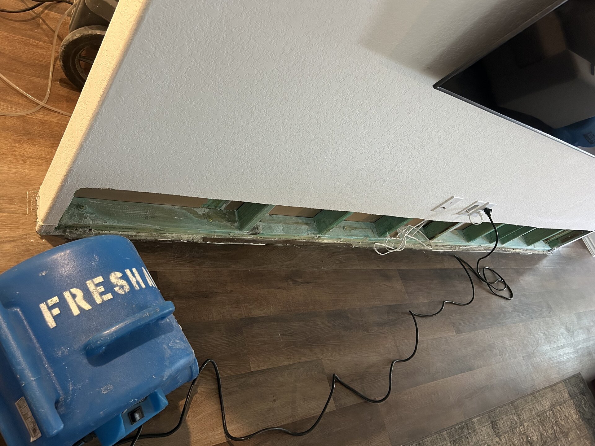Fresh Air air mover drying a wall cut open above the baseboard to expose the studs