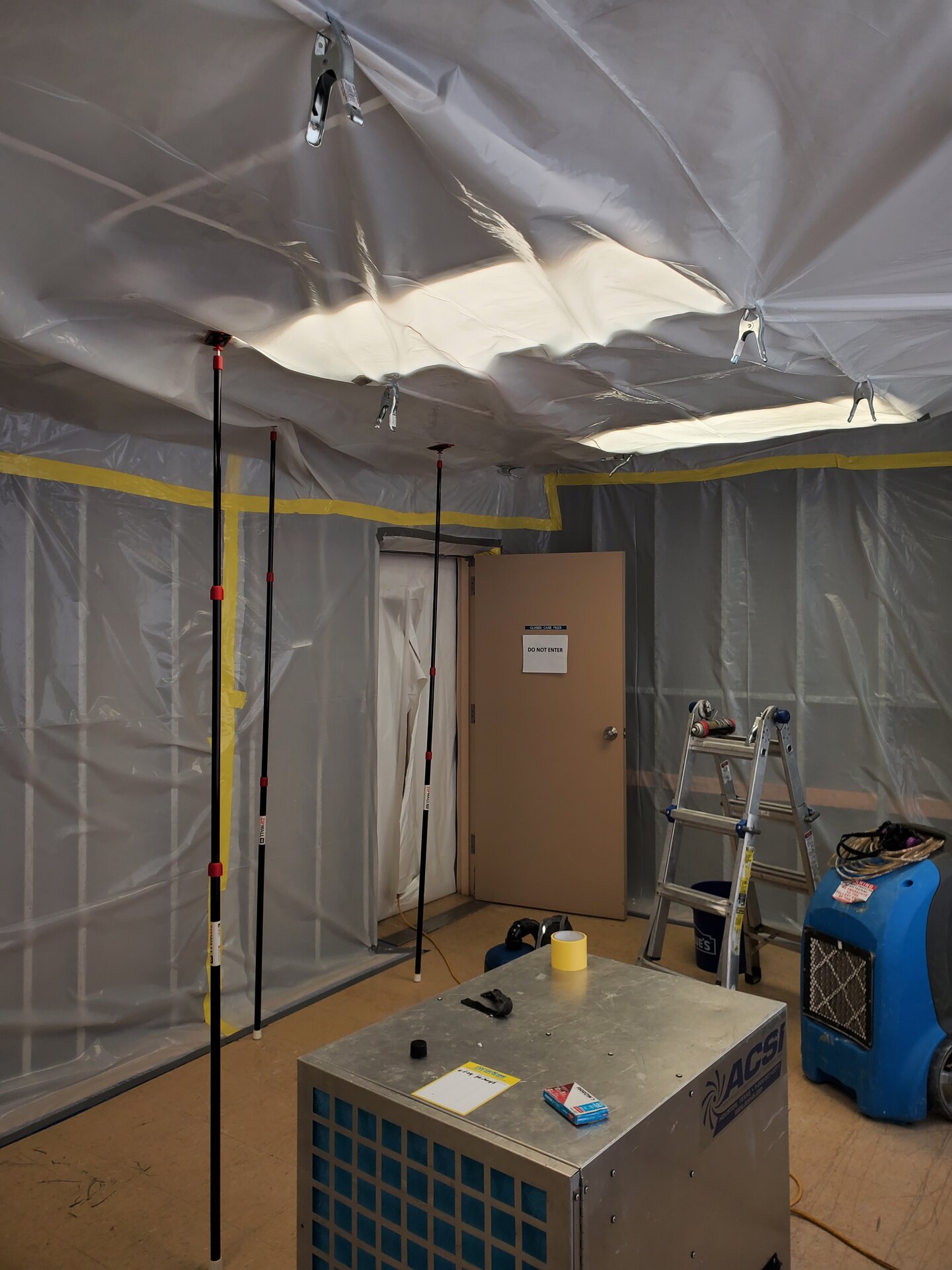 Full-room containment with a Do Not Enter sign on the door and a HEPA air scrubber running