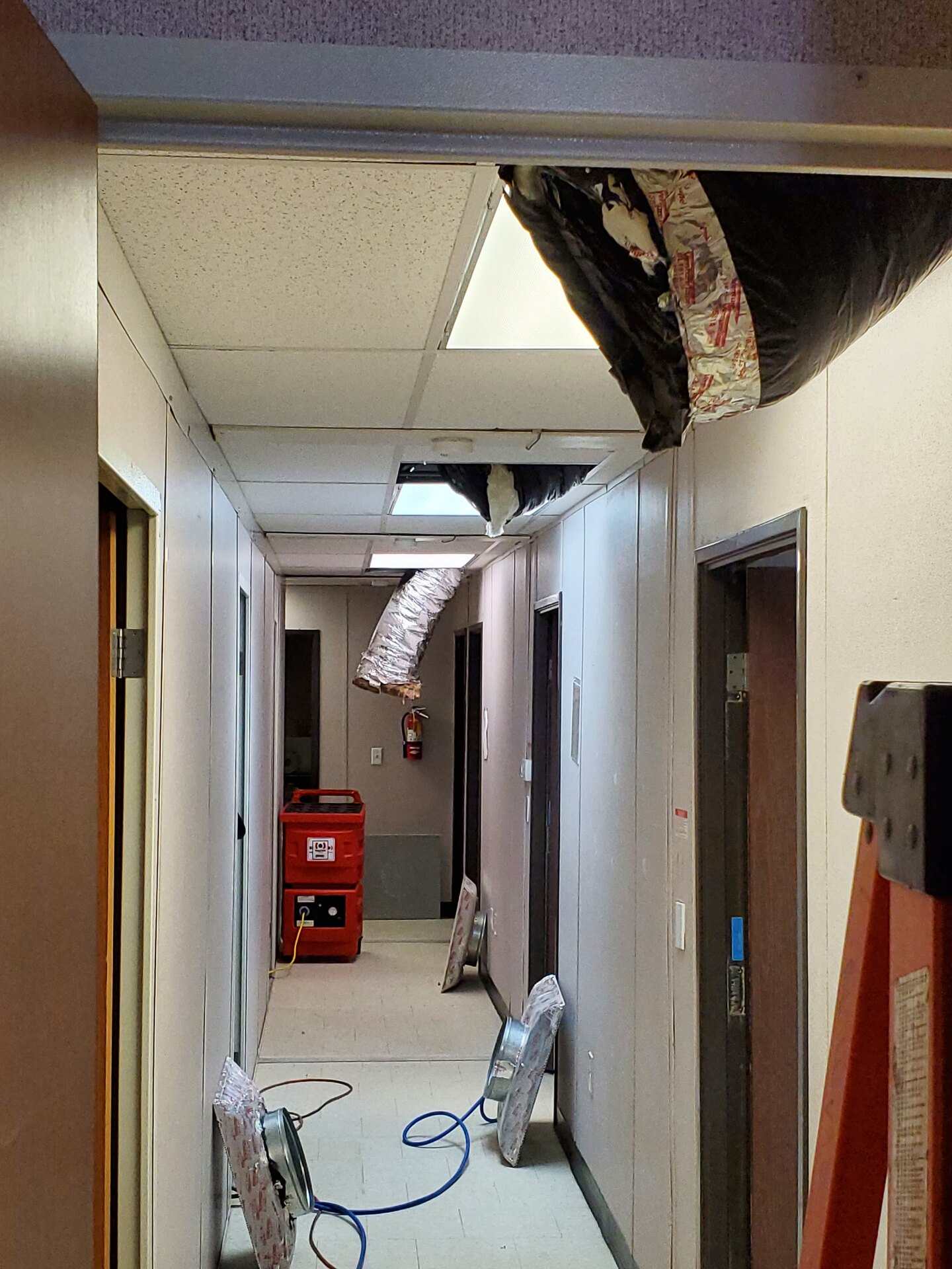 Commercial corridor with collapsed insulated ductwork hanging from the ceiling and air movers running