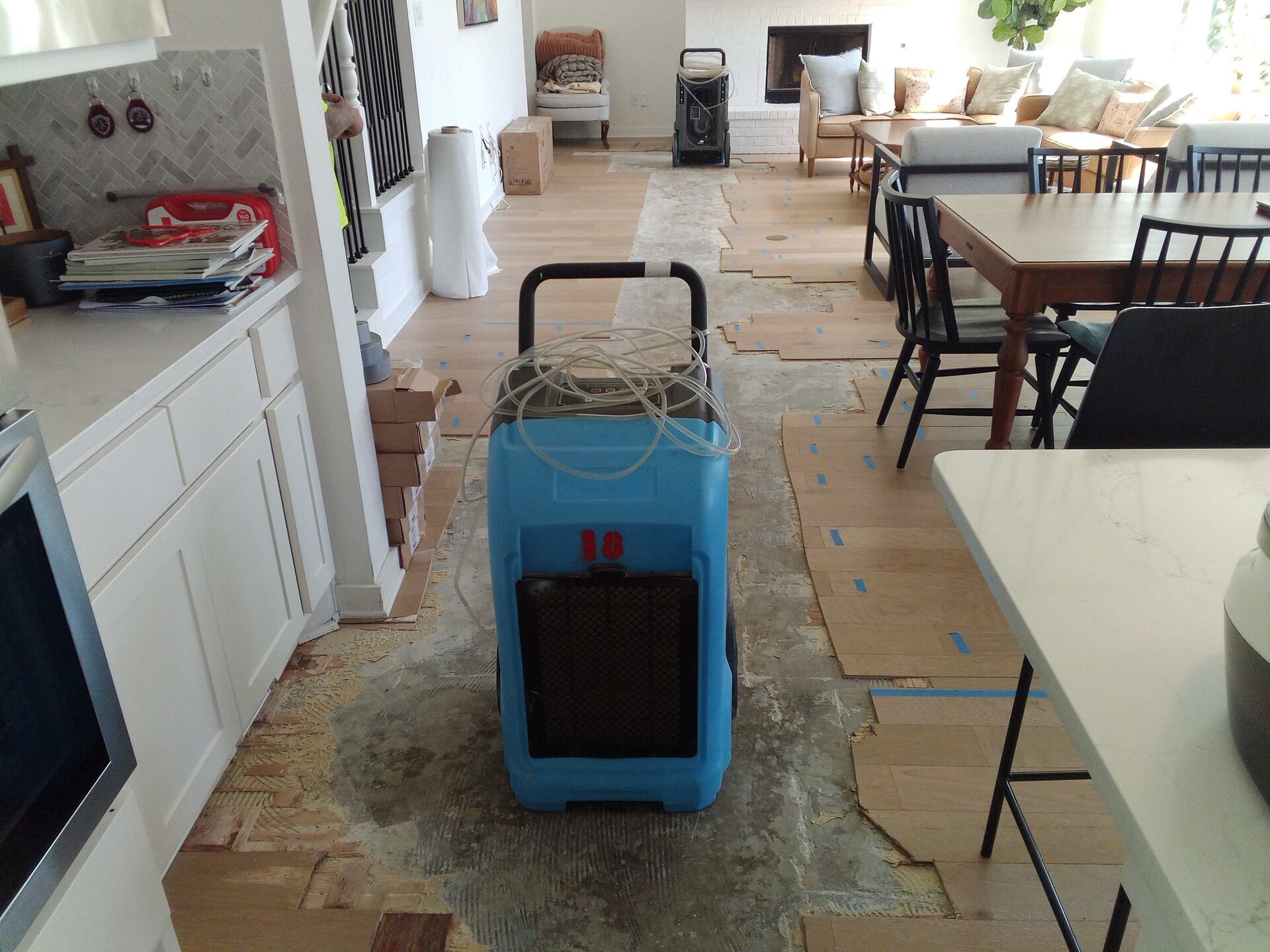 Hardwood planking pulled up across a kitchen and dining room with a commercial dehumidifier drying the subfloor