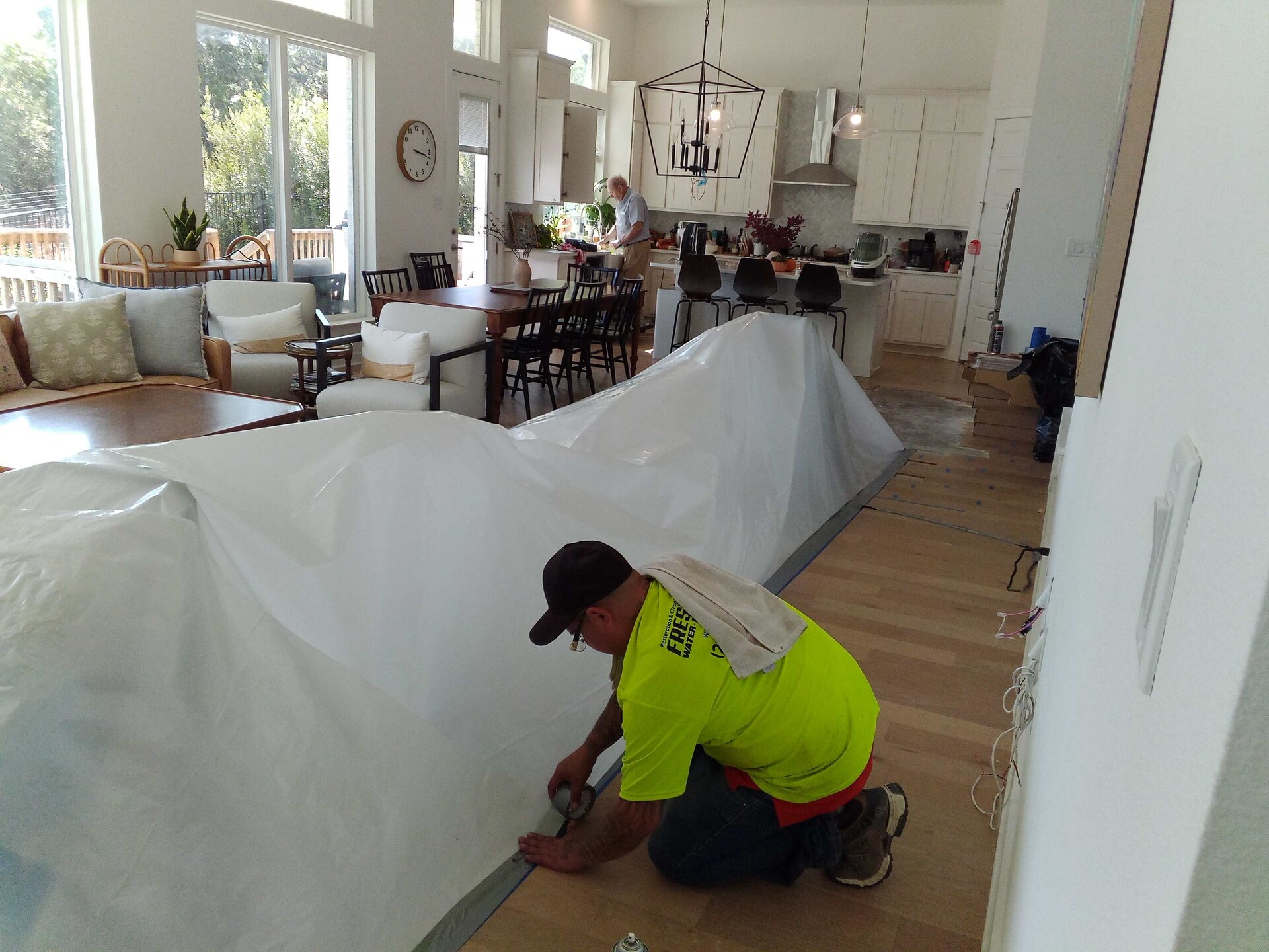 Fresh Air technician in a branded high-visibility shirt taping containment plastic to the floor of an open-plan home
