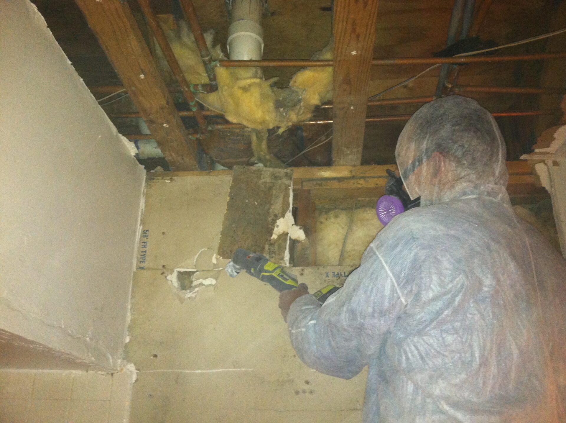 Fresh Air technician in a protective suit and respirator cutting out water-damaged ceiling drywall