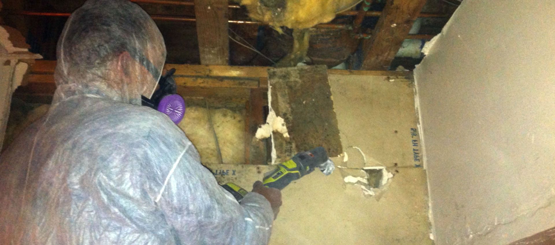 Fresh Air technician in a protective suit cutting out mold-damaged drywall