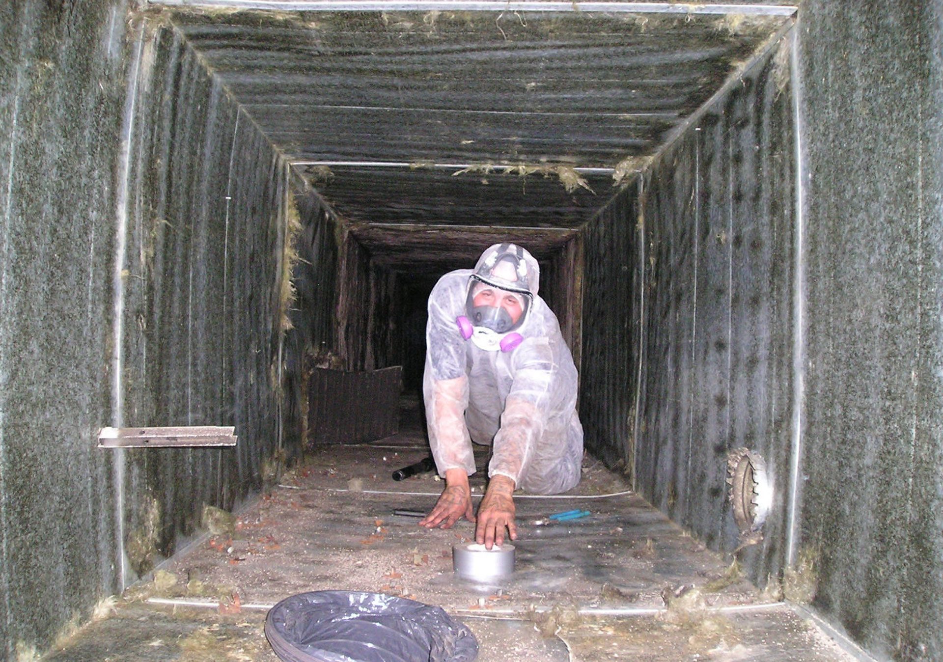 Fresh Air technician in a protective suit and respirator cleaning inside a large commercial air duct